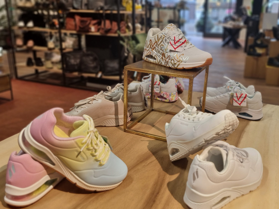 Verschiedene Sneaker auf einem Tisch in einem Laden, farbenfroh und stilvoll präsentiert.