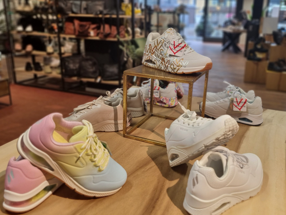 Verschiedene Sneaker auf einem Tisch in einem Laden, farbenfroh und stilvoll präsentiert.