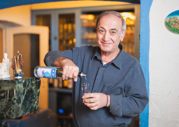 Lächelnder Mann mit grauen Haaren schenkt ein Getränk in ein Glas an einer Bar aus.