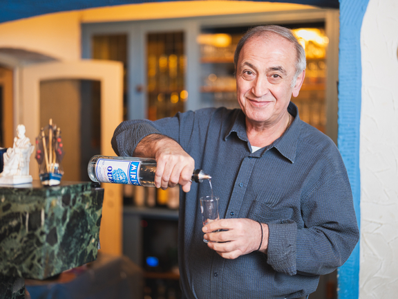 Lächelnder Mann mit grauen Haaren schenkt ein Getränk in ein Glas an einer Bar aus.