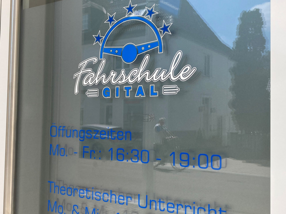 Fenster mit beschrifteter Öffnungszeiten und Hinweis auf Theorieunterricht einer Fahrschule.