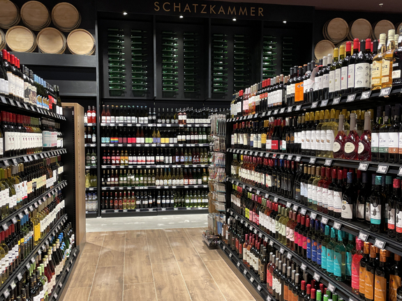 Weinregal in einem Geschäft, mit Regalen voller Weinflaschen und einem verkaufsfördernden Bereich im Hintergrund.