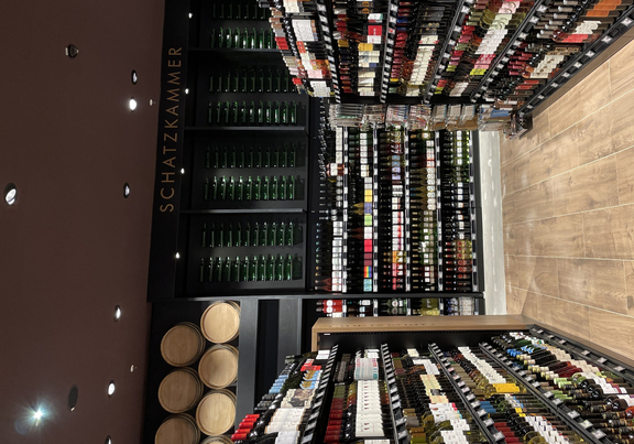 Weinregal in einem Geschäft, mit Regalen voller Weinflaschen und einem verkaufsfördernden Bereich im Hintergrund.