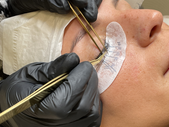 Nahaufnahme einer Frau, die eine Augenbrauen- oder Wimpernbehandlung erhält, Hände mit Handschuhen arbeiten sorgfältig.