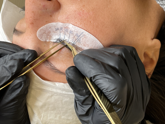 Nahaufnahme einer Frau, die eine Augenbrauen- oder Wimpernbehandlung erhält, Hände mit Handschuhen arbeiten sorgfältig.