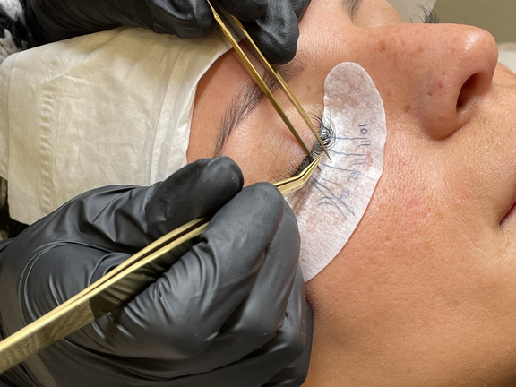 Nahaufnahme einer Frau, die eine Augenbrauen- oder Wimpernbehandlung erhält, Hände mit Handschuhen arbeiten sorgfältig.