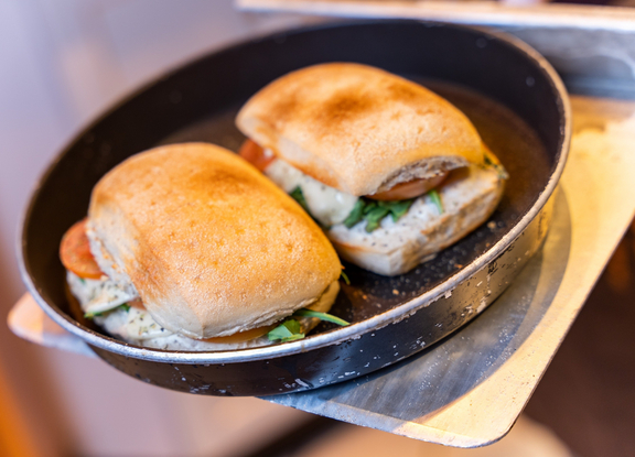 Zwei frisch zubereitete Sandwiches in einer Pfanne, auf einem Teller, mit gegrilltem Gemüse und frischen Kräutern.