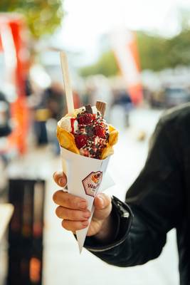 Ein Hand hält eine Waffeltüte mit Eis, Schokolade und einem Topping aus Erdbeeren und Süßigkeiten.