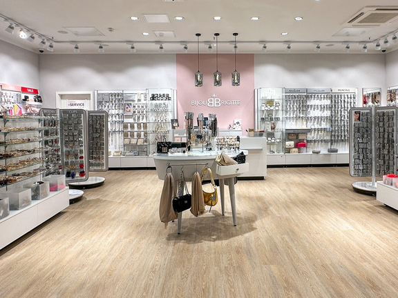 Innenansicht eines Modegeschäfts mit Kleidung und Accessoires auf weißen Regalen, gut beleuchtet mit Holzfußboden.