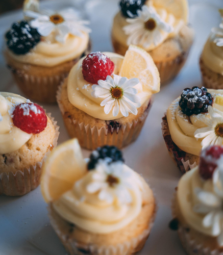 Bunte Cupcakes mit Sahne, Beeren, Zitronenscheiben und essbaren Blumen auf einem Teller.